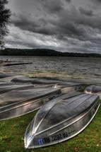 flipped rental boats resting on a lake shore as storm clouds approach 