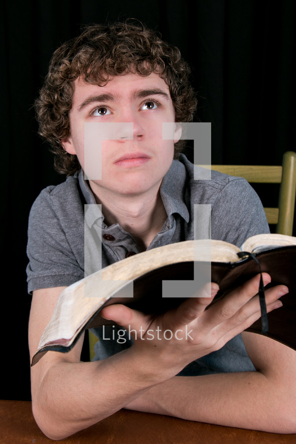 Teen reading the Bible at a wooden table.