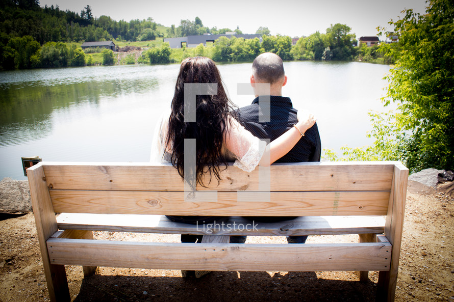 Couple sitting on a park bench by a lake.