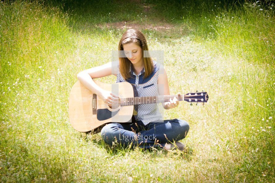 woman sitting in a field playing her guitar