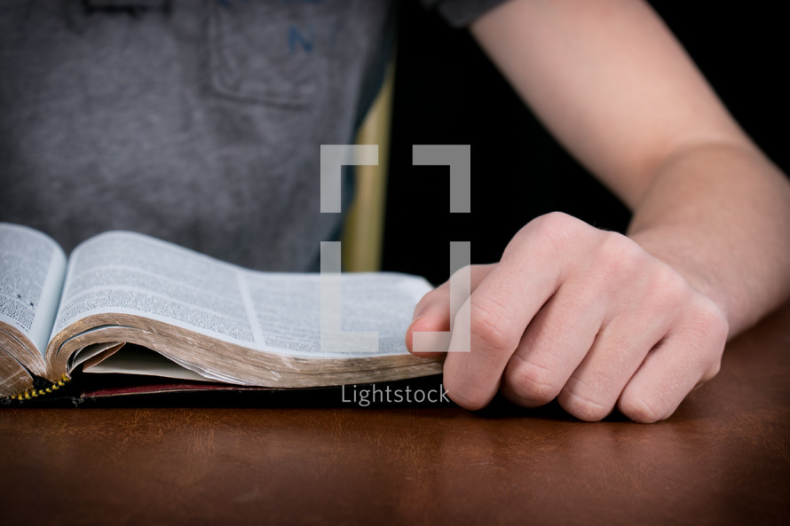 Teen reading the Bible on a wood table.