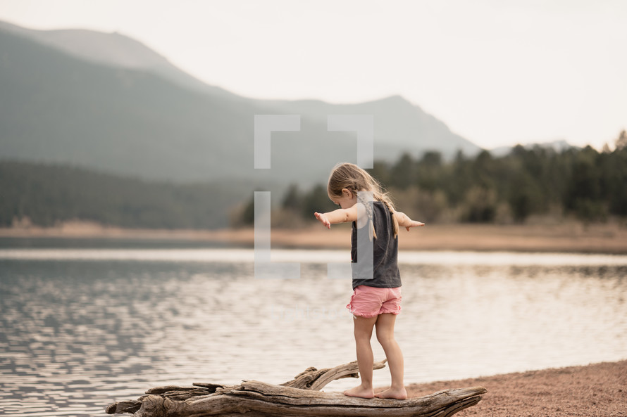 a little girl standing on a lake shore 