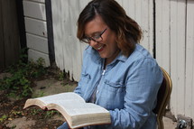 a woman in a chair reading a Bible outdoors 