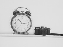 Vintage alarm clock and camera on a shelf.