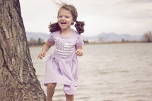 a girl laughing running beside a lake shore 