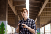 a young man standing under an overpass holding a camera 