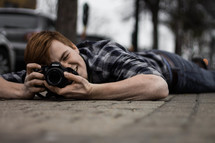 a man lying on a sidewalk taking a picture 