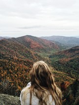 woman sitting on a mountaintop looking out at the view 