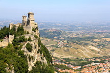 a castle on a mountainside over a valley village 