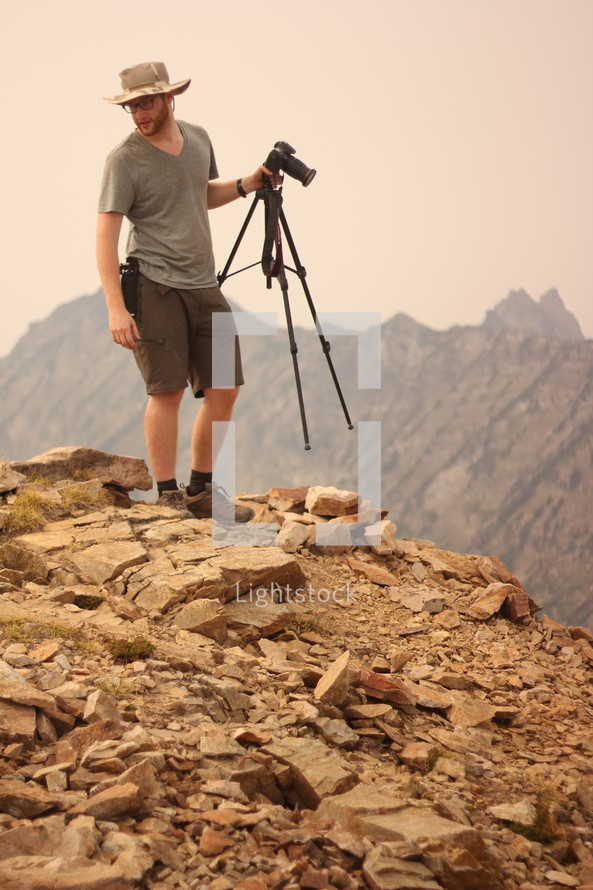 a man holding a camera on top of a mountain 