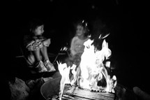girl sitting around a fire at night 