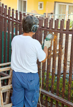 Worker cuts iron bars of a fence with grinder.