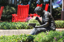 A bronze statue of a man reading a book, red rocking chairs behind him