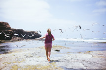 a woman chasing seagulls on a beach 
