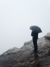 man standing on a rock holding an umbrella 