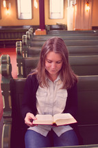 woman sitting in church pews reading a Bible 