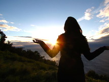 Silhouette of a woman appreciating the sunrise over the mountains.