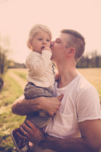 Father holding and kissing child outside.