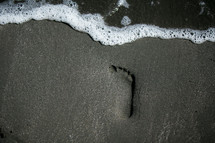 tide washing onto a beach and a footprint in the sand 
