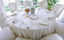 White lace tablecloth on large round table set for a wedding