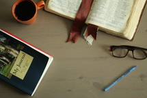 an open Bible, journal, and coffee mug on a coffee table