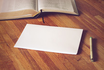 open Bible, envelopes, and pen on a wood floor 