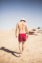 man in a swim suit walking on a beach 