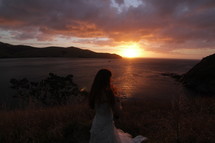 Bride standing outside overlooking the ocean at sunset.