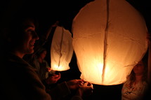 friends lighting floating paper lanterns at night 