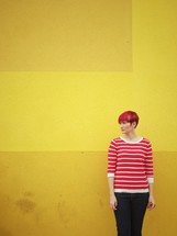 A woman standing in front of a yellow wall. 