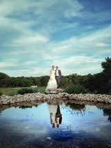 Bride and groom and a pond in the foreground. 