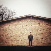 A man standing in front a brick house. 