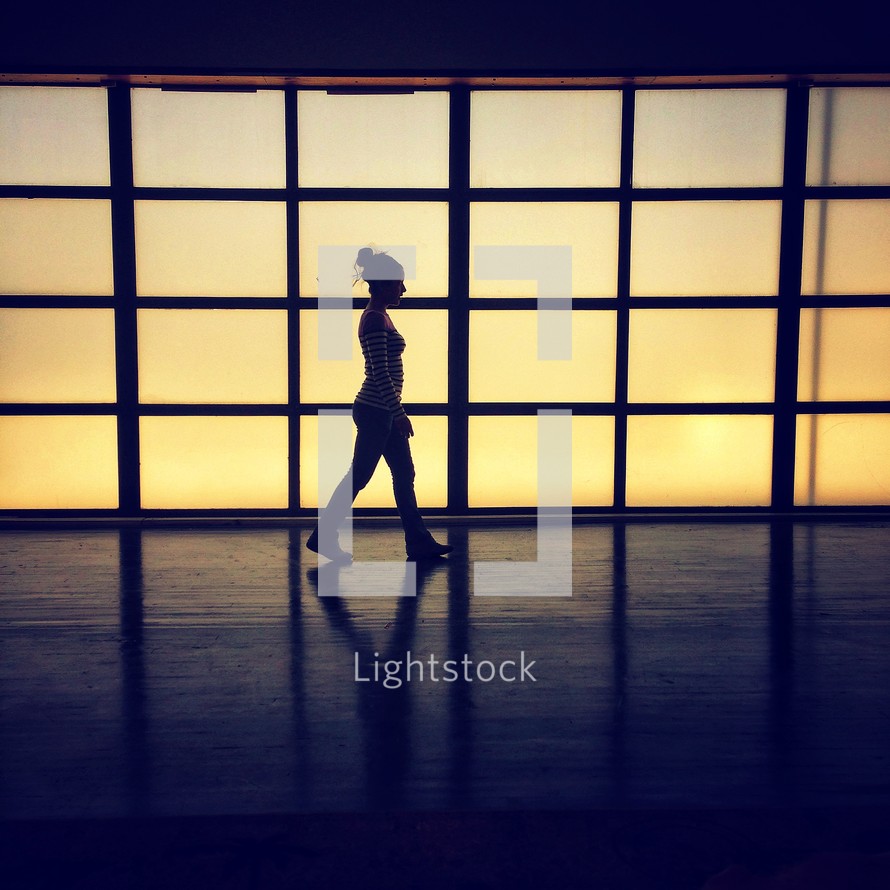 A silhouette of a woman walking in an airport terminal. 