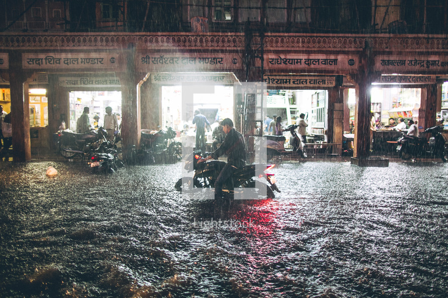 A man riding a motorcycle on a flooded street. 
