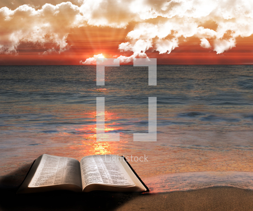 Open Bible on a beach at sunrise as the tide washes over it 