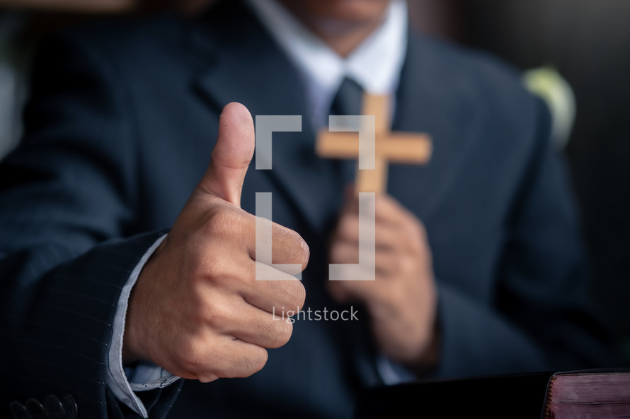 Close up thumbs up of pastor, with hands holding a cross at background