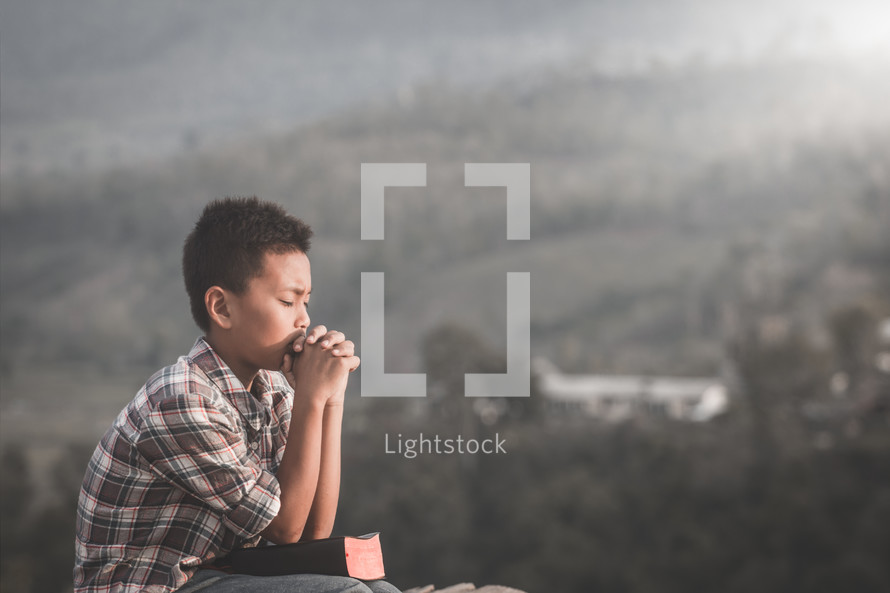 a boy praying outdoors 