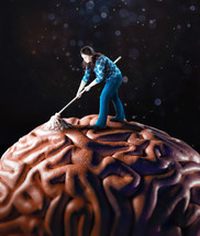 A woman stands on top of a large brain with a mop to clearn.