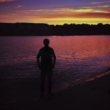 silhouette of a man standing in front of ripples in water at sunset