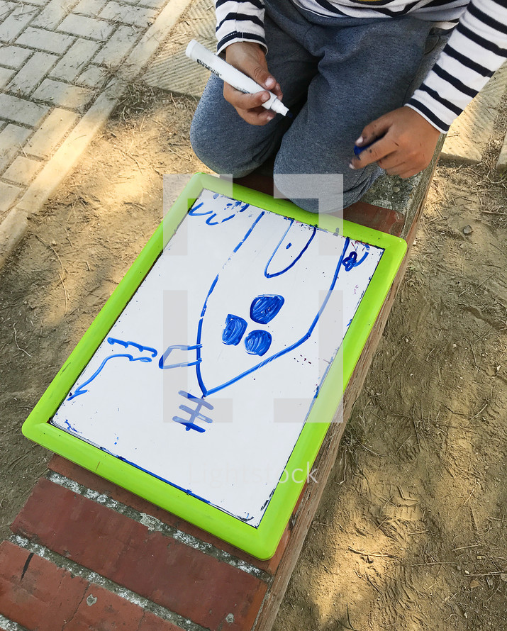child coloring on a whiteboard outdoors 