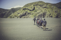 line of people backpacking across a sandy beach 