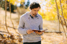 a man standing reading a Bible on a fall day 