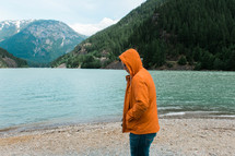 a man in an orange jacket standing on a lake shore 