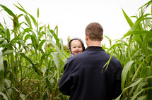 a father carrying his son through a tall corn field 