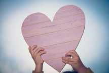 a child's hand up a wooden heart 