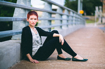 Woman sitting against the railing of an overpass. 