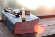 watch and wooden cross on a closed Bible 