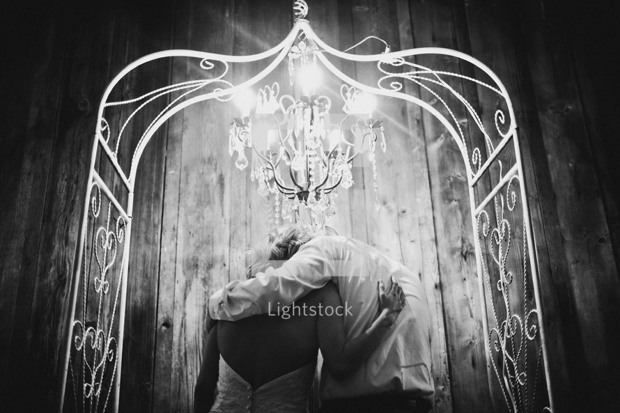 bride and groom under a chandelier and arbor