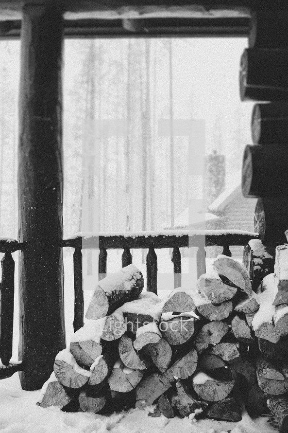 Firewood stacked on the snow covered porch of a log cabin.