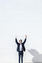 a man standing in front of a white wall with hands raised 